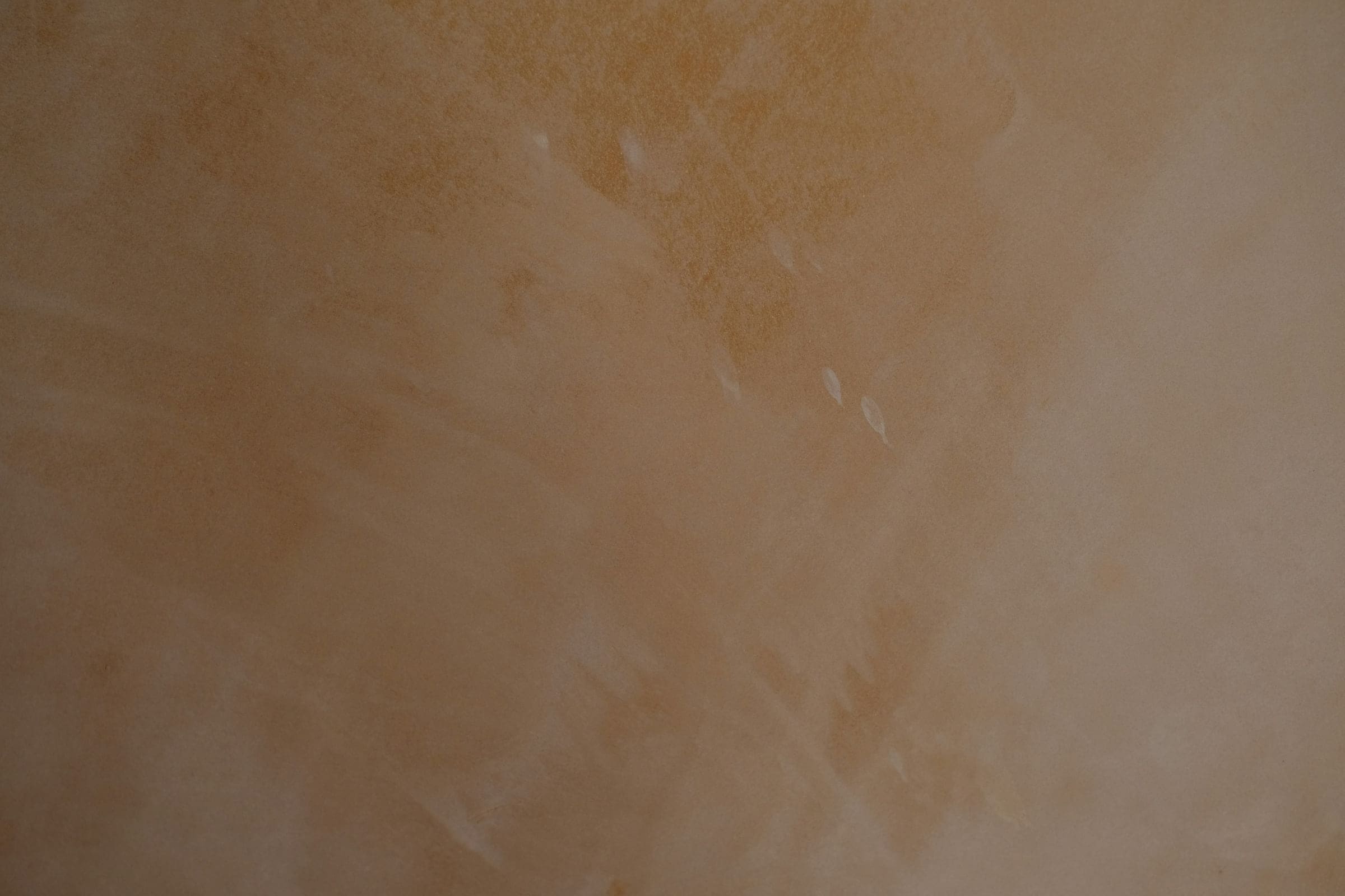 Gros plan d’un mur en marmorino ocre et miel, poli à la spatule, avec des nuances de pierre et de légers reflets