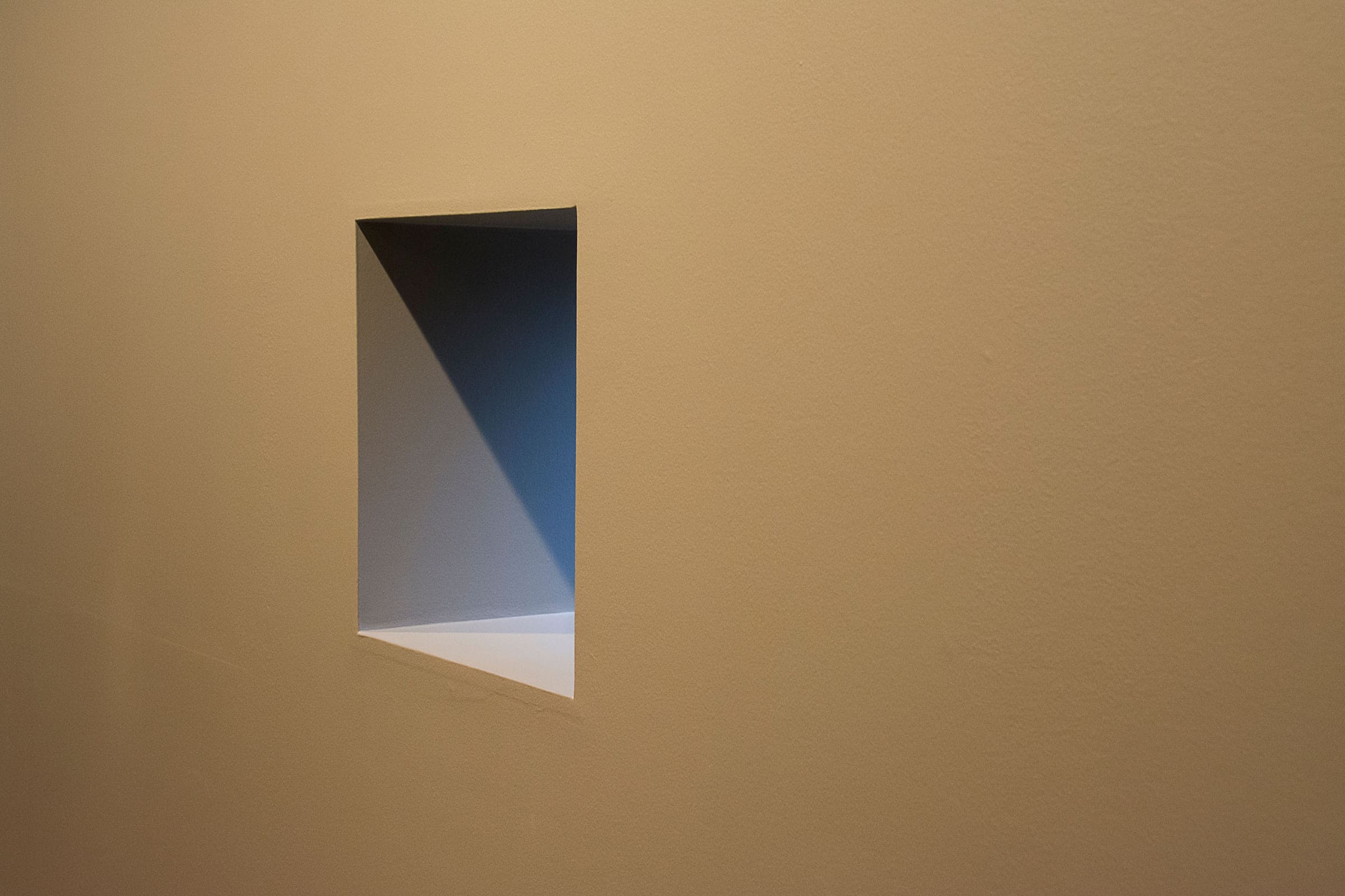 Niche rectangulaire creusée dans un mur enduit couleur sable, arêtes vives et ombre nette dans la lumière rasante
