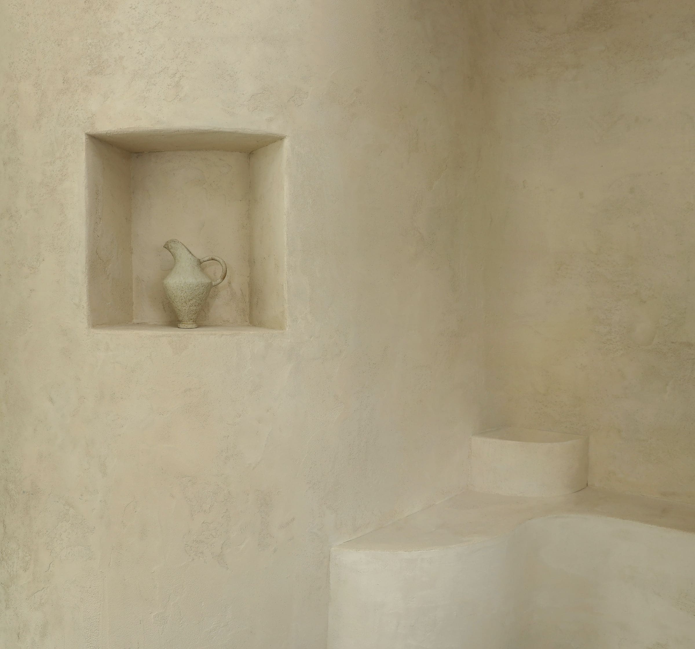 Mur de douche en tadelakt crème avec une niche creusée dans l’enduit et un banc arrondi, surface satinée et lisse